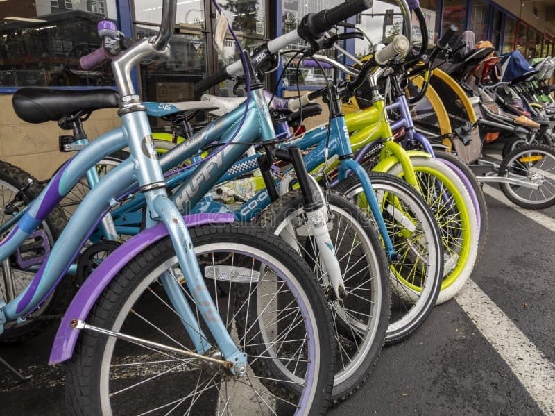 Fila de bicicletas coloridas alineadas frente a una tienda con carritos de bebé al fondo.