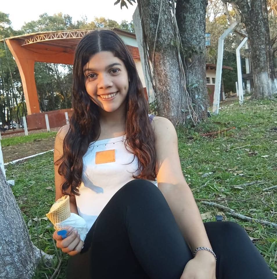 Joven sonriente con hoyuelos sentada en el césped de un parque sosteniendo un helado.