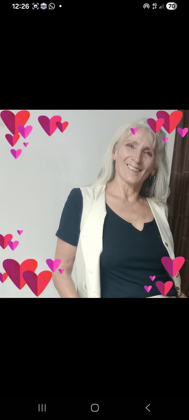 Mujer sonriente de cabello largo claro con chaleco blanco y corazones rosas y rojos.